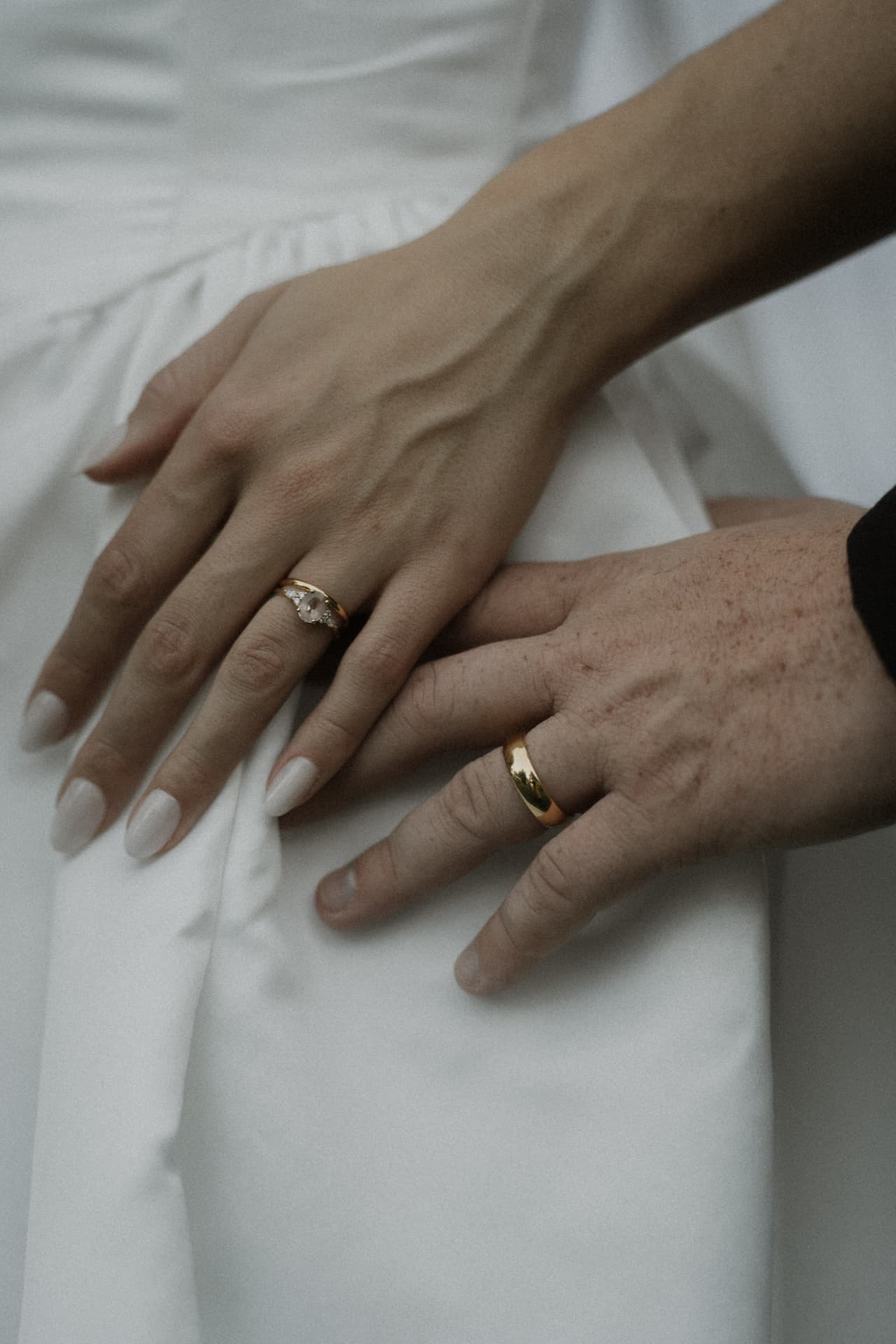 Close-up of a bride and groom’s hands with wedding rings on her white dress
