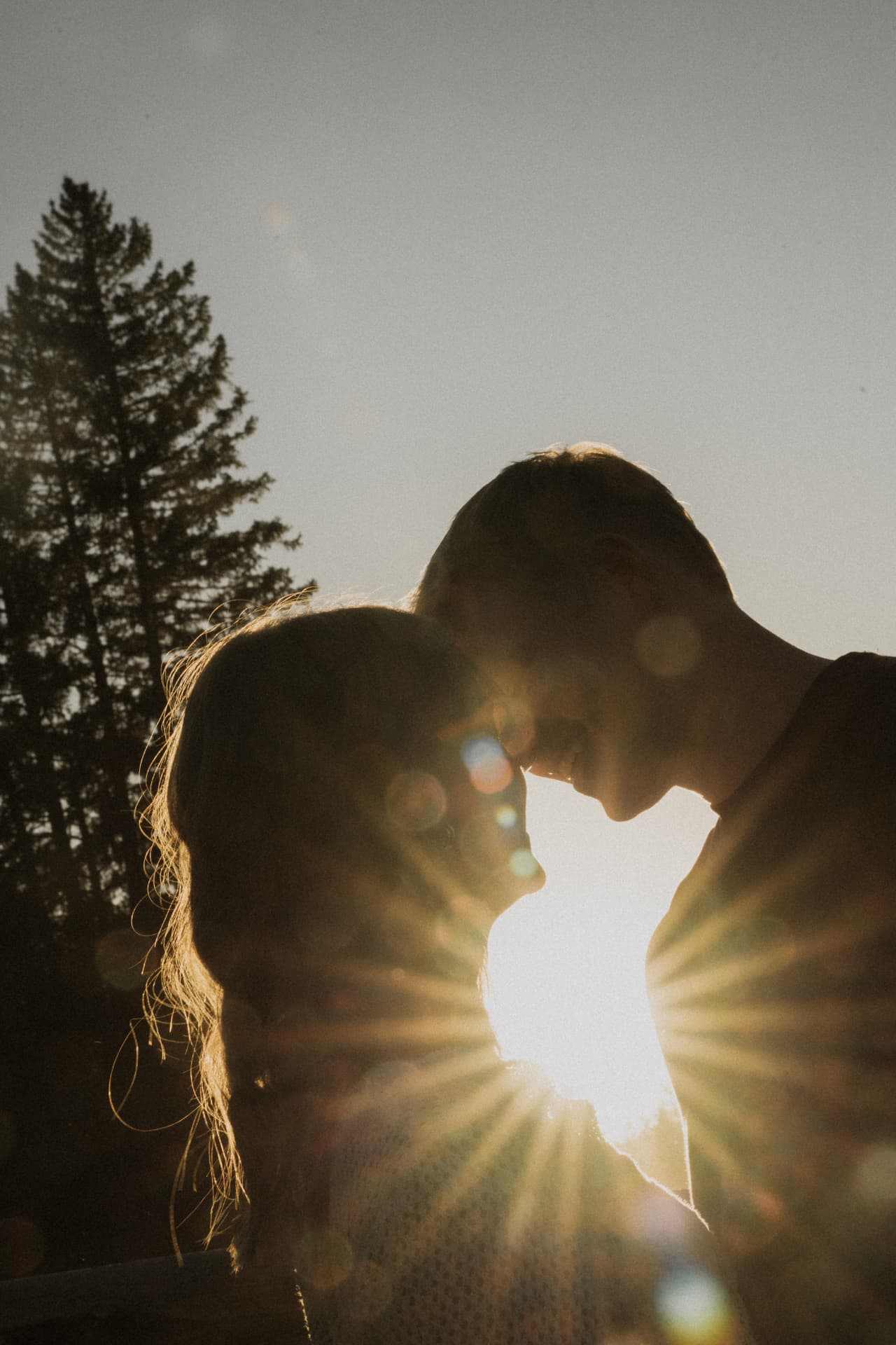 A couple silhouetted forehead to forehead with the sun bursting between them