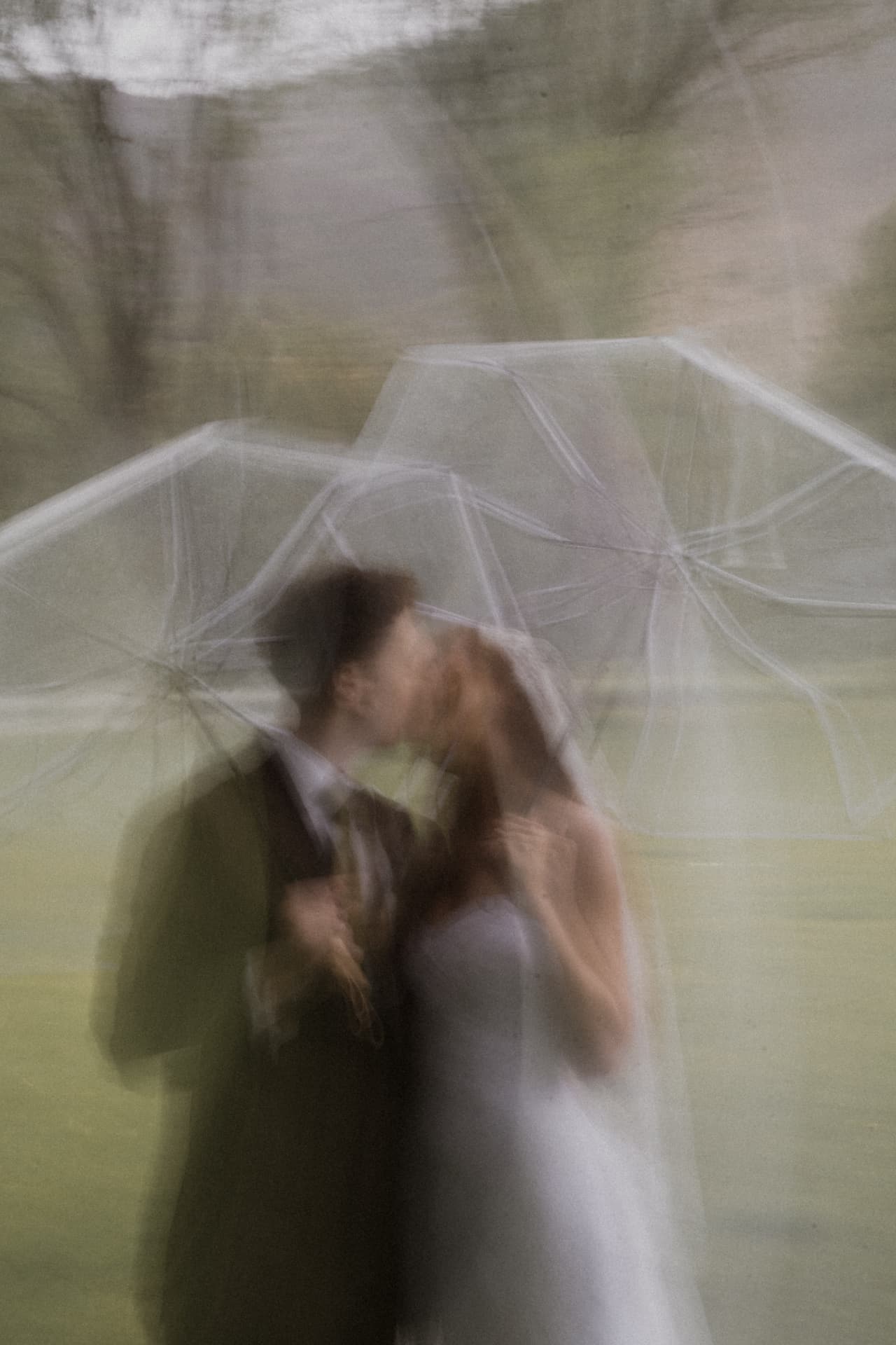A motion-blurred couple kissing beneath clear umbrellas in the rain