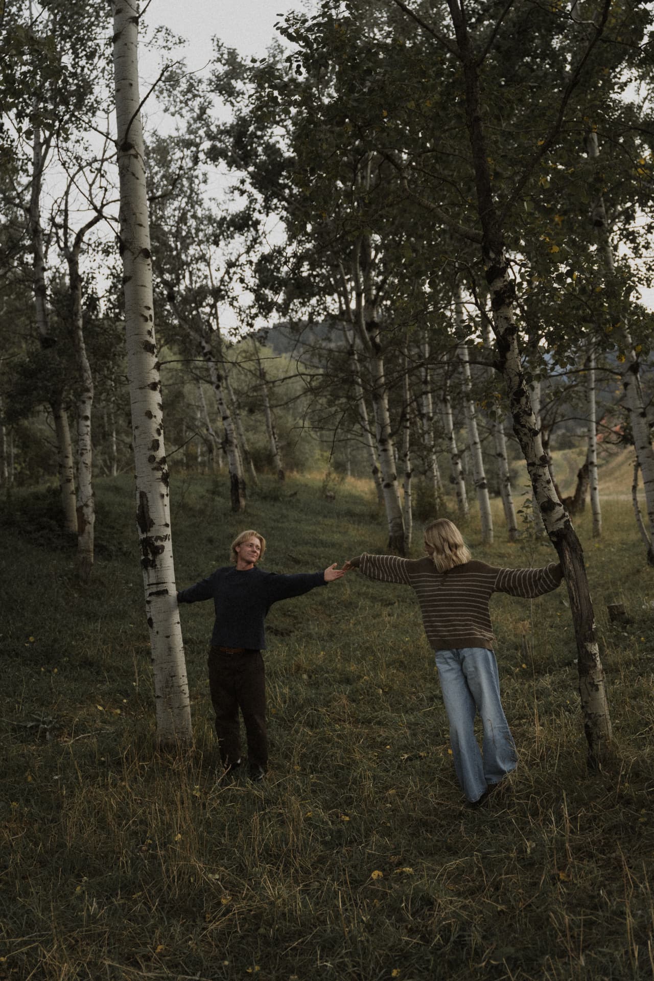 A couple holding hands between tall trees in the woods