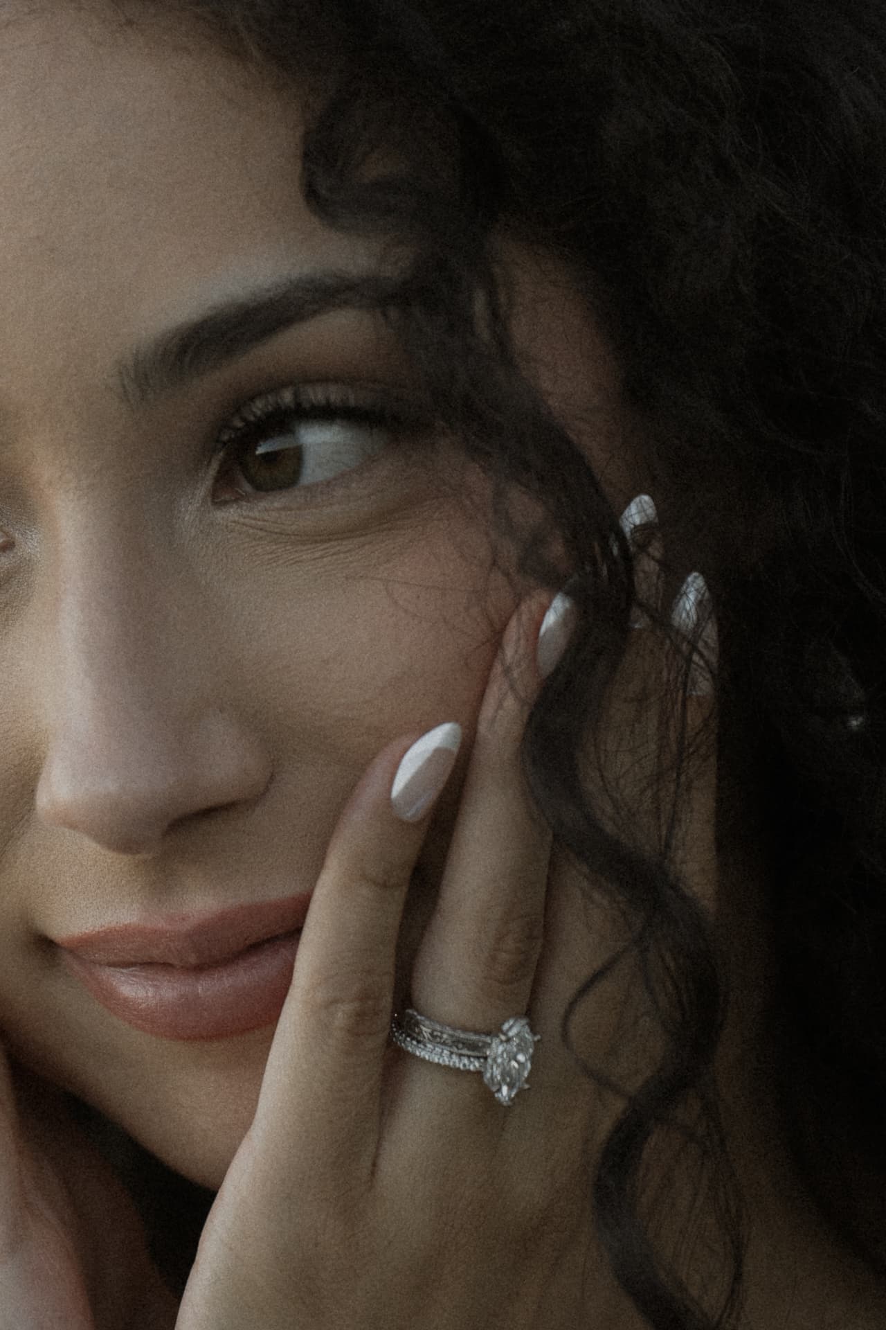 Close-up of a woman’s face and hand wearing an engagement ring