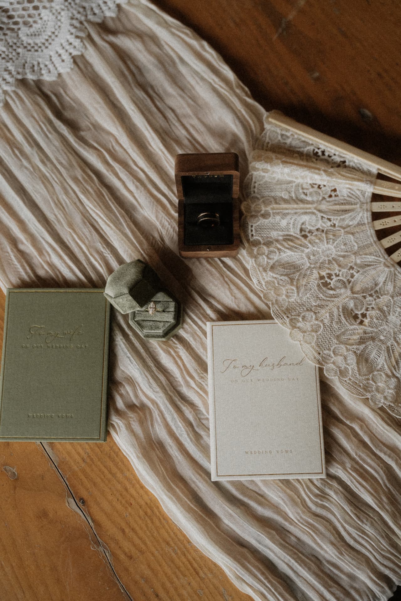 Vow books, rings, and a lace fan laid out on a wooden table