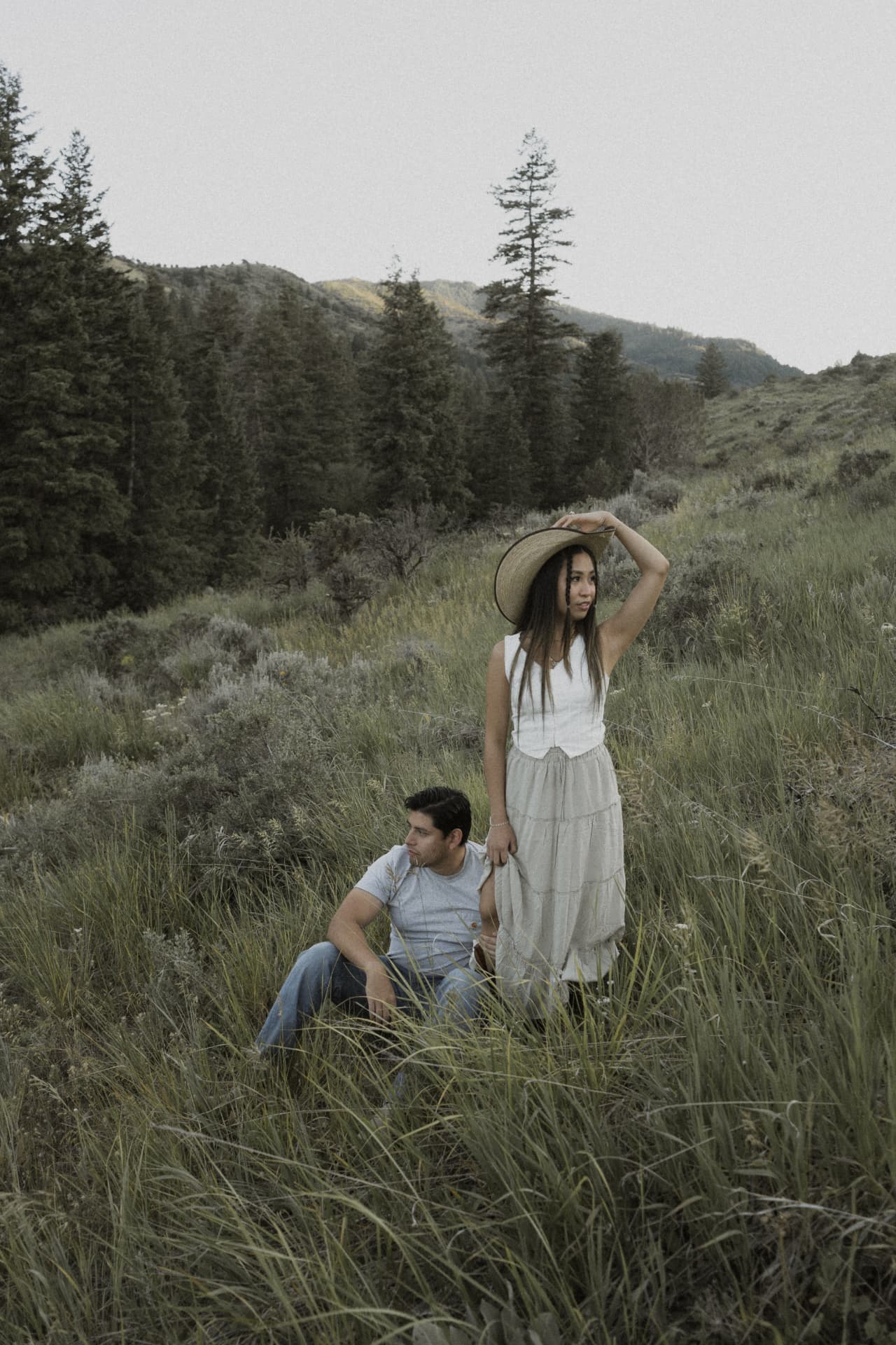 A couple in tall sagebrush grass, her straw hat against the wind